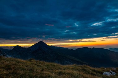 Gün doğumu dağlarda, güneş bulutları boyuyor.