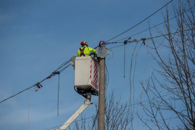 Bergamo, İtalya, 27 Ocak 2026: Elektrik teknisyeni kaldırma platformu kullanarak bir üstten elektrik hattı üzerinde bakım yapıyor. Enerji altyapısında güvenlik ekipmanları ve yüksek görünürlüklü giysilerle çalışıyor..