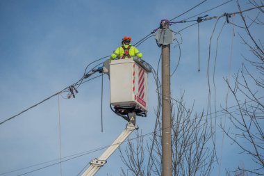 Bergamo, İtalya, 27 Ocak 2026: Elektrik teknisyeni kaldırma platformu kullanarak bir üstten elektrik hattı üzerinde bakım yapıyor. Enerji altyapısında güvenlik ekipmanları ve yüksek görünürlüklü giysilerle çalışıyor..