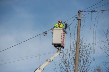 Bergamo, İtalya, 27 Ocak 2026: Elektrik teknisyeni kaldırma platformu kullanarak bir üstten elektrik hattı üzerinde bakım yapıyor. Enerji altyapısında güvenlik ekipmanları ve yüksek görünürlüklü giysilerle çalışıyor..