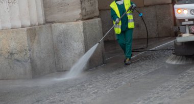 Milan İtalya 27 Şubat 2026: Bir belediye hizmetleri çalışanı yüksek basınçlı su jetiyle yol yüzeyini temizliyor, yüksek görünürlüklü güvenlik giysileri giyiyor