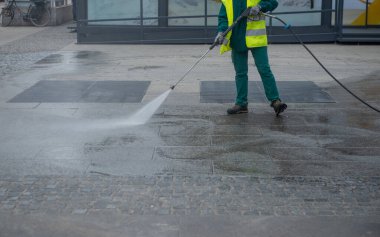 Milan İtalya 27 Şubat 2026: Bir belediye hizmetleri çalışanı yüksek basınçlı su jetiyle yol yüzeyini temizliyor, yüksek görünürlüklü güvenlik giysileri giyiyor