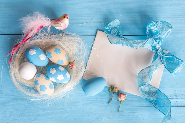 Easter eggs in the nest on blue wooden background with note fore your text — Stock Photo, Image