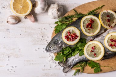 Çeşitli malzemelerle pişirme balık yemek. Limon, sarımsak, otlar ve baharatlar kesme tahtası, üstten görünüm üzerinde ham Gökkuşağı alabalığı. Sağlıklı gıda veya diyet beslenme kavramı