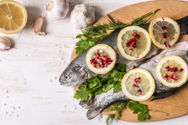 Çeşitli malzemelerle pişirme balık yemek. Limon, sarımsak, otlar ve baharatlar kesme tahtası, üstten görünüm üzerinde ham Gökkuşağı alabalığı. Sağlıklı gıda veya diyet beslenme kavramı