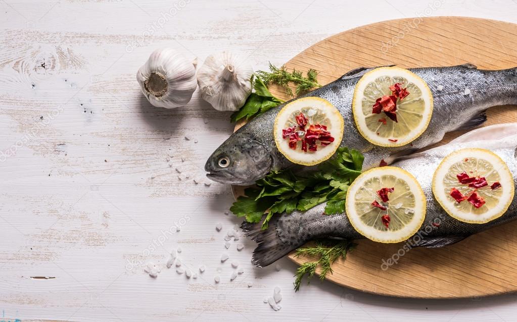 Fish dish cooking with various ingredients. Raw rainbow trout with lemon, garlic ,herbs and spices on cutting board , top view. Healthy food or diet nutrition concept