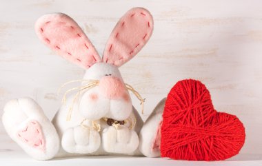 Yumuşak oyuncak beyaz tavşanı beyaz zemin üzerine yün bir kalp. Sevgililer günü kavramı. Çocuk oyuncakları