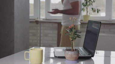 Dairedeki pencerenin yanında bir adam telefonla konuşuyor. Genç adam telefonda bir şey açıklıyor ve ellerini sallıyor. Dairedeki çalışma masası.