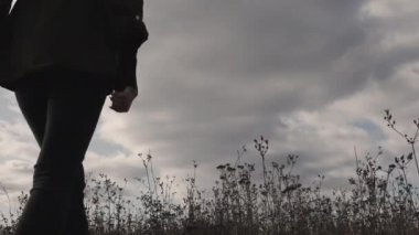 Doğada bir kız, manzaranın tadını çıkaran yalnız üzgün bir kız, yüksek çimlerde yürüyen ve gökyüzüne bakan bir kadın.