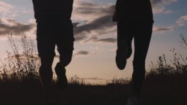 Doğada koşan insanların silueti, mutlu çift neşe gösteriyor, aşk çifti gün batımında koşuyor, erkek ve kız neşeli.