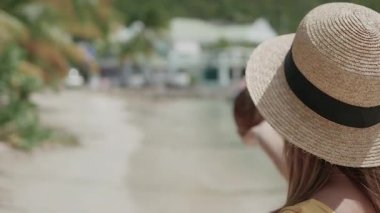 Elinde hindistan cevizi olan bir kız, kumsalda şapkalı bir kız, tatil köyünde bir kadın.