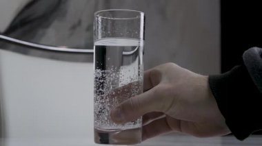 Beyaz bir masada bardaktaki su, bir adam masaya bir bardak su koyar, şeffaf bir bardakta su içer.