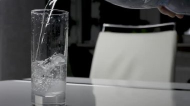 Bardağa maden suyu akıyor. Plastik şişeden bardağa doğal su dökülüyor. Mutfak masasında su içmek.