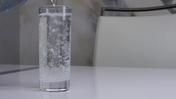 白い背景に青いガラス瓶からミネラルウォーターを入れ 白いキッチンテーブルの上にガラスのミネラルウォーター 泡で水を飲む — ストック動画