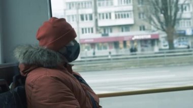 Tıbbi maskeli bir adam şehir aracında oturur ve pencereden dışarı bakar, virüsten korunma konsepti, otobüsteki maskeli bir adam.