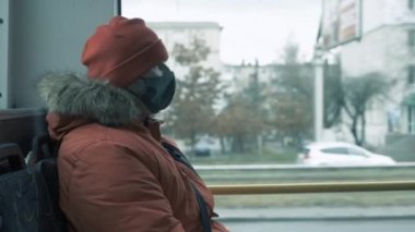 Yüzünde koruyucu tıbbi maske takan, virüsten korunan, kışlık ceketli ve otobüsteki şapkalı bir adam pencereden dışarı bakıyor. Salgın konsepti 