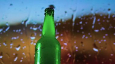 Barın üzerinde bir şişe bira kayıyordu. Şişedeki hafif bira yağmur damlalarının arka planında, yağmurlu arka planda bira