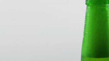 Şişede hafif bira. Şişe açacağıyla bir bira şişesi aç, yeşil bira şişesi, beyaz arka planda yakın plan. Şişeye bira köpüğü dökülüyor.
