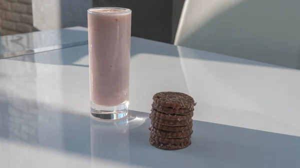 水果酸奶在一个玻璃杯与巧克力糕点在一个白色厨房桌子上 牛奶饮料 一杯草莓酸奶 — 图库照片