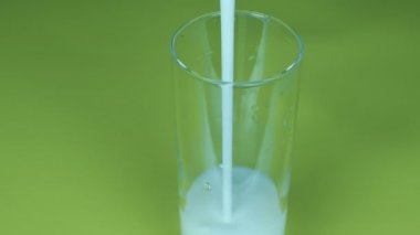 Kefir, yoğurt bardağa, güzel bir süt akışı, yeşil arka plan. Yakın plan, taze süt ürünü.