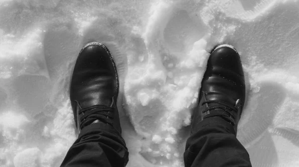 Boots in the snow, a man stands in a snow-white black-and-white photo, top view with his feet in the snow