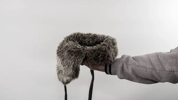 Holding hat in hand begging on a white background, place to insert the product in the hat. A man is waiting for handouts in a hat with earflaps. The homeless man asks