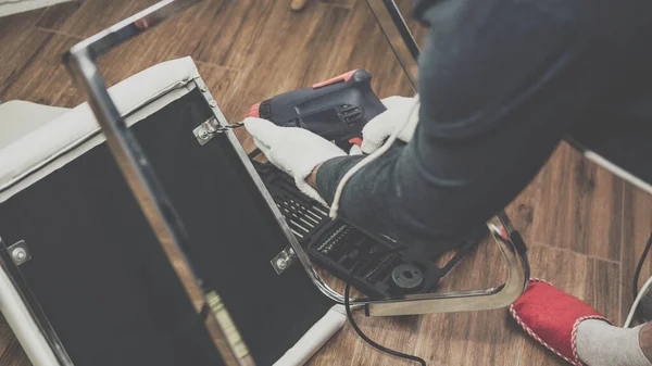 A man in a red slipper repairs furniture, a man drills furniture, a young guy repairs a chair.