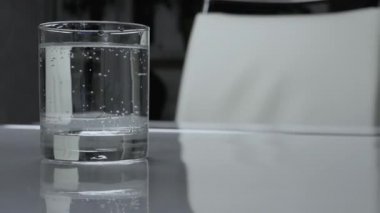 Beyaz mutfak masasında bir bardak maden suyu, cam bardakta su içmek.
