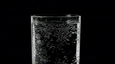 Siyah zemin üzerinde bir bardakta suya yakın çekim, bardakta maden suyu, soda, bardakta köpük.