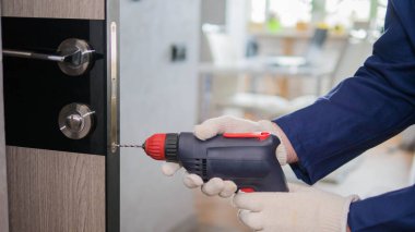 A carpenter repairs an interior door, a craftsman with an electric drill in his hands