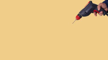 An electric drill in a man's hand on a bright beautiful background, a construction tool on a yellow background.