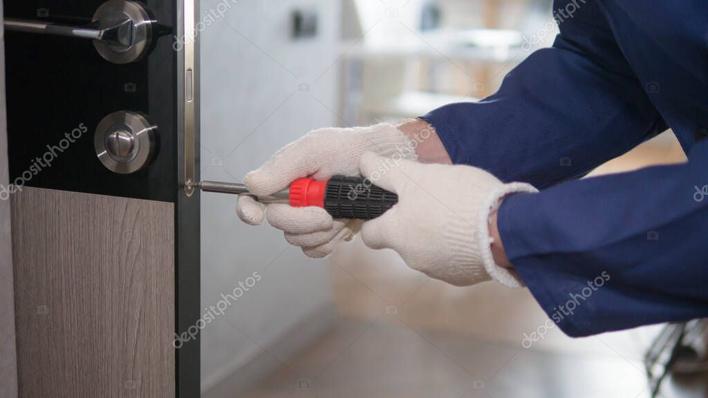 The interior door is being repaired by a handyman, a man in a special uniform with a screwdriver in his hands, a carpenter at work