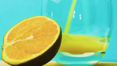 Mavi arka plana sarı limonata dök. Şeffaf bardakta meyve suyu. Bardakta doğal meyve suyu olan portakal dilimi.