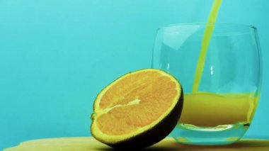 Mavi arka plana sarı limonata dök. Şeffaf bardakta meyve suyu. Portakal suyu ile portakal dilimi