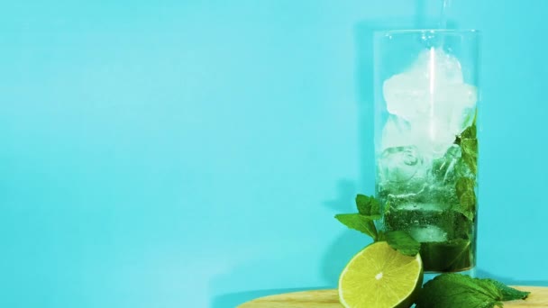コピースペース モヒート 冷却ドリンクのクローズアップ フルーティなアルコールと青の背景にガラスに氷でミントドリンクを注ぐ 夏の冷たい飲み物 — ストック動画
