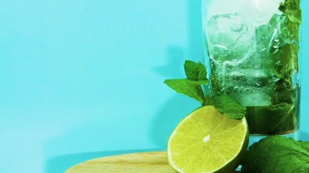 ライムスライス コピースペース モヒート 冷却ドリンクのクローズアップ フルーティなアルコールと青の背景にガラスに氷でミントドリンクを注ぐ 夏の冷たい飲み物 — ストック動画
