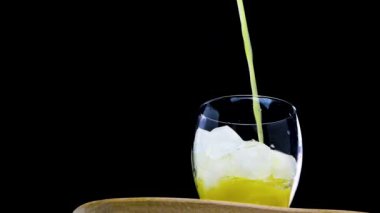 Ağır çekim. Siyah arka planda bir bardağa portakal suyu dök, sarı limonata yakın plan bardağa dökülür.