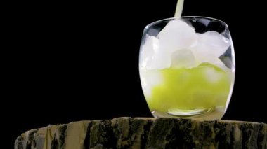 Siyah bir arka planda, ağır çekimde, sarı limonata, şeffaf bir bardağa multivitamin içeceği dökün.
