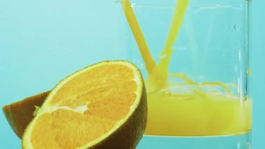 Portakal suyu ve bir dilim portakal suyu mavi arka planda şeffaf bir bardağa dökülüyor. Sarı limonata.