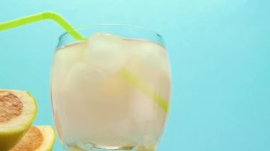 Juice with a pipe in a glass and ice, a grapefruit cocktail, an alcoholic drink in a glass on a solid wood rack on a blue background