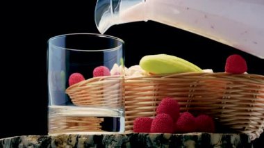 Pour fruit yogurt into a glass on a black background studio shot, natural yogurt in a glass and with fruits in a wicker basket. Milk product.