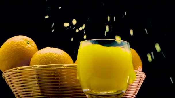 黒を基調とした氷の入ったガラスの中でジューシーなオレンジジュース オレンジジュースのグラスに氷を投げる — ストック動画