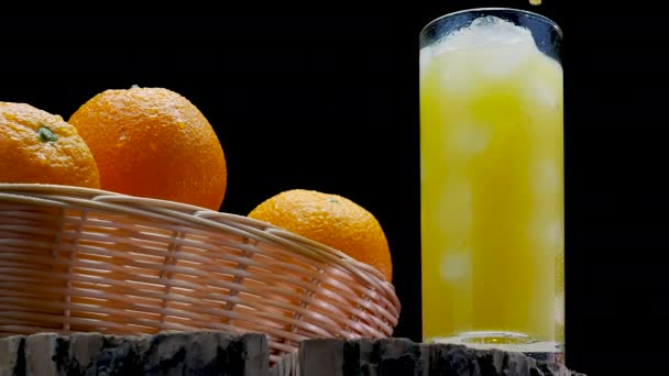 杯子里有稻草 背景是黑色的 夏天水果和冰块一起喝 新鲜橙子放在一个篮子里 篮子里有新鲜挤榨的果汁在木板上 — 图库视频影像