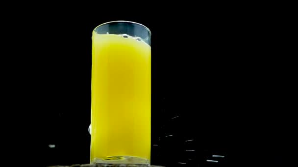 黄色のレモネードに氷を投げ 黒の背景にガラスのオレンジジュースのスプラッシュ オレンジフルーツカクテル — ストック動画