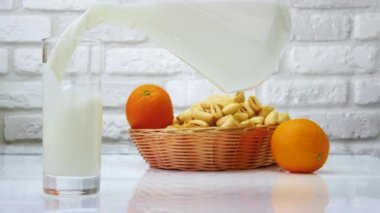Sütü sürahiden bardağa dök. Sütü, meyve ve hamur işlerini beyaz mutfak masasına bırak. Beyaz tuğla bir duvara süt dök.