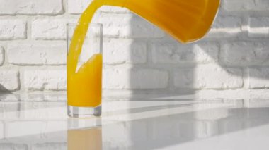 Sarı limonatayı sürahide beyaz tuğladan bir arka plana dök. Taze portakal suyu. Beyaz mutfak masasında meyveli portakal suyu olan bir bardak.