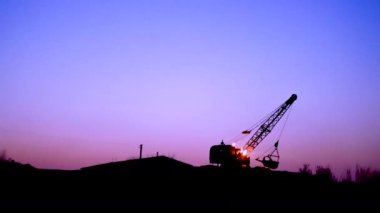 Kazıcı gün batımında kazıyor. Traktör çukur kazıyor. Yürüyen merdiven kovayla kazıyor.