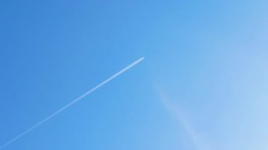 Mavi gökyüzündeki uçak irtifada ters yöne dönüyor. Uçaktan havadaki yakıt izleri.