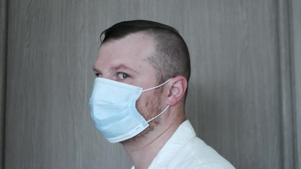 木製の背景に彼の顔に医療マスクと白いジャケットでハンサムな医者の肖像画 その男は顔を医療マスクで覆った 幸せな男はウイルスから保護されています 健康コンセプト — ストック動画