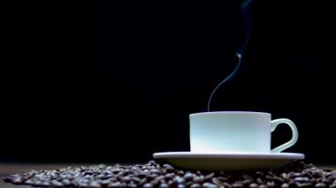 Siyah arka planda dumanlı bir fincan kahve. Siyah arka planda bir fincan kahve ile kahve çekirdeği.